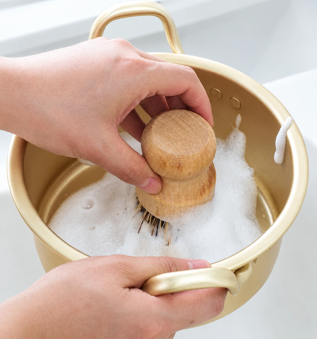 Hands scrubbing a pot with the coarse coir dish brush